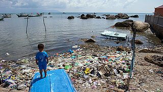 Ein Junge steht an einem Strand voller Plastikmüll