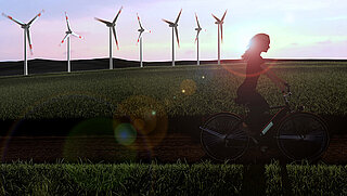 A woman rides a bicycle in front of wind turbines.