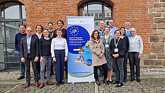 Mehrere Personen stehen rechts und links von einem Rollup 