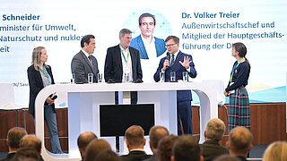 Mehrere Personen stehen hinter einem Stehtisch auf einer Bühne. 