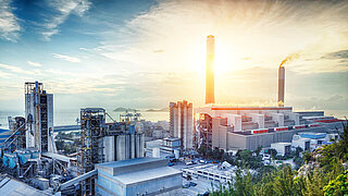 Eine Industrielandschaft (Fabriken und Schornsteine) vor einem Sonnenaufgang 