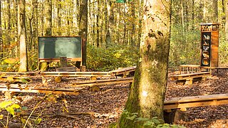 Eine Schultafel und Sitzbänke im Wald