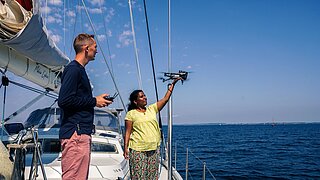 Zwei Personen auf einem Segelboot starten eine Drohne über dem Meer