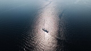 Segelboot auf ruhiger See mit Sonnenreflexion auf der Wasseroberfläche
