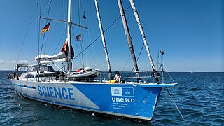 ZU sehen ist ein blau-silbernes Segelboot auf dem Meer, auf dem sich eine Person befindet.