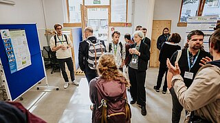 Mehrere Personen stehen vor einem Poster und sprechen miteinander. 
