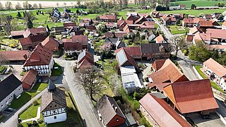 Foto von oben auf eine Ofrtschaft, man sieht diverse Häuser, Straßen, Bäume und Grünflächen