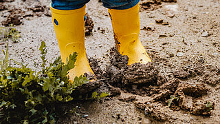 Kinderbeine mit Gummistiefeln im Schlamm