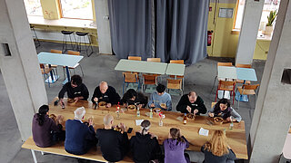 Mehrere Personen sitzen essend und sich unterhaltend an einem Tisch