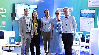 5 Personen stehen vor einem Messestand