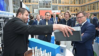 Mehrere Personen stehen an einem Tisch und schauen sich Gegenstände an. Eine Person hält eine Art Kastenin der Hand. 