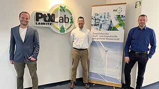 Vertreter des PtX Lab Lausitz und der Fraunhofer Einrichtung IEG stehen vor einem großen Logo des PtX Lab Lausitz