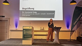 Die Geschäftsführerin der ZUG, Dr. Constanze Haug, steht auf einem Podium mit einem Mikrofon in der Hand