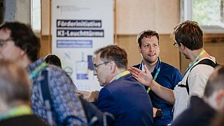 Mehrere Personen im Gespräch, im Hintergrund steht ein Rollup