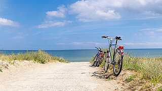 Ein Strandweg, im Hintergrund ist das Meer zu sehen, am Rand steht ein Fahrrad.