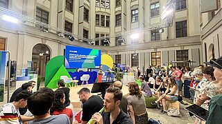 Menschen sitzen vor der Bühne und hören zu.
