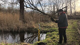 Ein Projektmitarbeiter liest die Messpegel einer wiedervernässten Fläche aus.