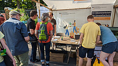 Mehrere Personen stehen an einem Messestand und schauen sich Informationen an