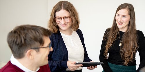 Ein Mann am Computer und zwei Frauen unterhalten sich
