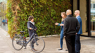 Eine Frau mit Fahrrad und drei weitere Personen vor einem Gebäude