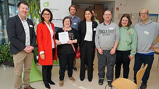 Mehrere Personen blicken in die Kamera. Eine hält eine Urkunde in der Hand. 