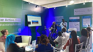 Zwei Personen stehen mit Mikros in der Hand vor einem Publikum