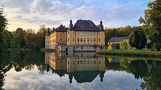 Das Wasserschloss Dyck spiegelt sich in einem ruhigen Teich