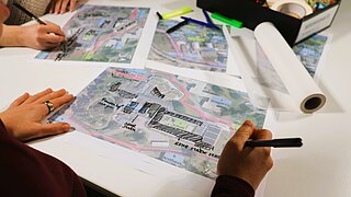 Auf einem weißen Tisch liegen mehrere Karten des Epilepsiezentrums in Kehl, auf denen von zwei Händen Pläne für Umbauarbeiten eingezeichnet werden.