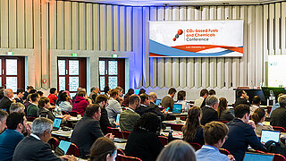 Viele Personen sitzen in einem Saal und verfolgen einen Vortrag.