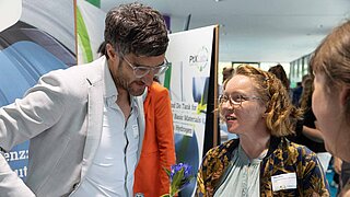 Eine Mitarbeiterin spricht zu einem Interessenten beim PtX Lab Lausitz Stand auf einer Messe