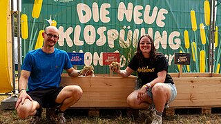 ein Mann und eine Frau sitzenvor einem Holzgefäß mit Biostreu