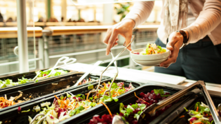 Ein Mensch befüllt seinen Teller an einer Salatbar.