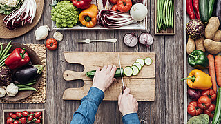 Person cuts fresh vegetables on wooden board