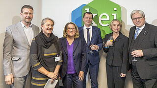 Sechs Personen stehen vor dem Wandschriftzug des KEIs bei dessen Eröffnung