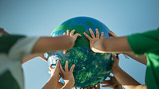 Children's hands holding up a planet in the open air