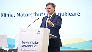 Ein Mann steht hinter einem Rednerpult und spricht in ein Mikro. 