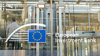 Schild mit dem Logo der Europäischen Investitionsbank an der modernen Glasfassade ihres Hauptsitzes.