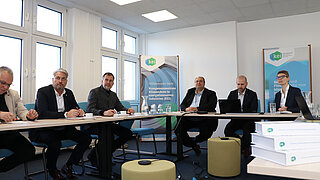 Bürgermeister, seine Kolleg*innen und Mitarbeitende aus Cottbus sitzen an Tischen und hören zu