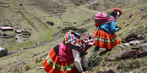 Two indigenous women in traditional clothing are climbing up a hill.