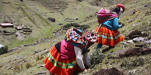 Zwei indigene Frauen in traditioneller Kleidung steigen einen Berg hinauf