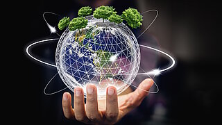 Hand hält eine digitale Erdkugel mit Bäumen auf der Oberfläche und leuchtenden Umlaufbahnen vor dunklem Hintergrund