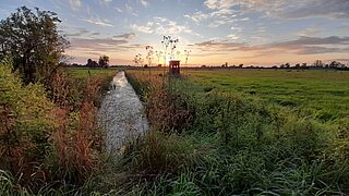 Eine Landschaft mit Graben, im Hintergrund geht die Sonne unter 