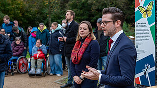 Mehrere Personen, darunter Kinder und Erwachsene, stehen vor einem Informationsschild mit dem Titel 'Es war einmal ein Parkplatz…', das die ökologische Umgestaltung des ehemaligen Bökelbergstadion-Parkplatzes am Spielkaulenweg beschreibt.