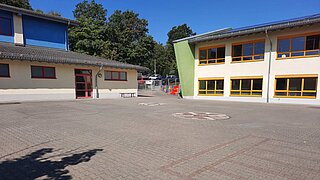 ein gepflasterter Schulhof mit zwei Gebäuden