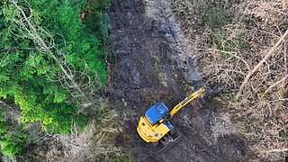 Eine Luftbildaufnahme zeigt einen Bagger in einer Waldschneise