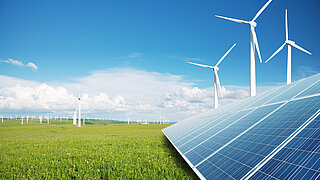 Wind- und Solaranlagen auf einer grünen Wiese vor blauem Himmel.