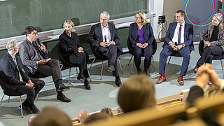 Eine Gruppe von Personen in Anzügen versammelt in einem Stuhlkreis die eine Diskussion führen