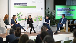 Mehrere Personen sitzen auf einer Bühne und sprechen, im Vordergrund Publikum