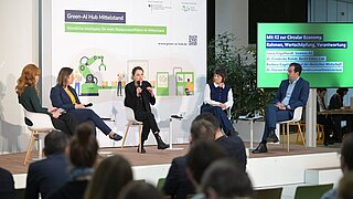 Mehrere Personen sitzen auf einer Bühne und sprechen, im Vordergrund Publikum