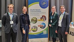 Vier Personen stehen links und rechts eines Rollup-Displays der LIFE-Beratungsstelle.